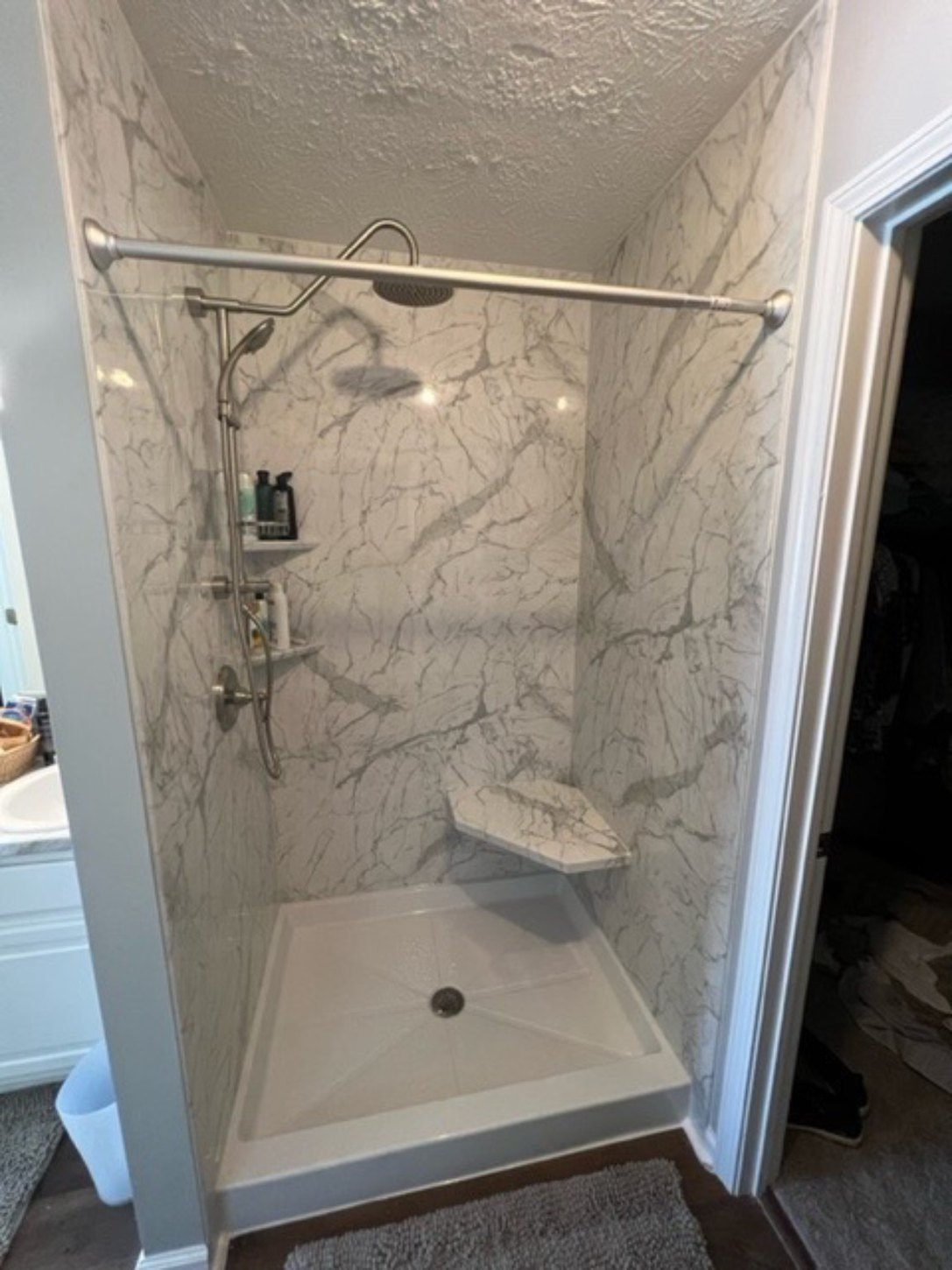Open marble-look shower with a corner seat, handheld shower, and low threshold